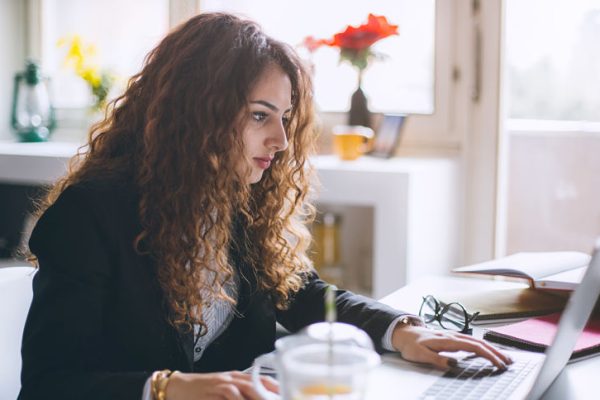 Stylish woman working in her modern office, using laptop, mobile phone, taking notes and searching the internet